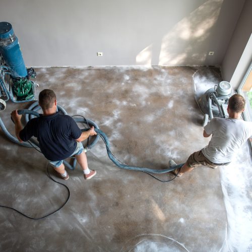 Construction workers in a family home living room that grind the concrete surface before applying epoxy flooring.Polyurethane and epoxy flooring.Concrete grinding.